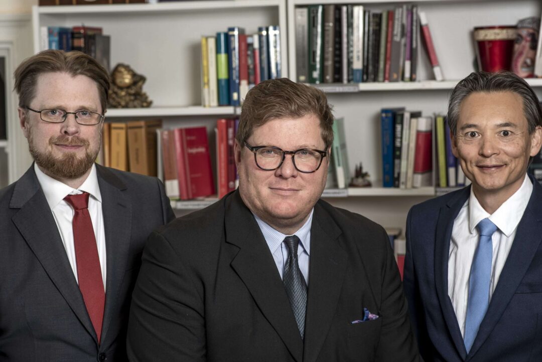 Tre jurister i kostym från Rättsakuten framför en bokhylla.