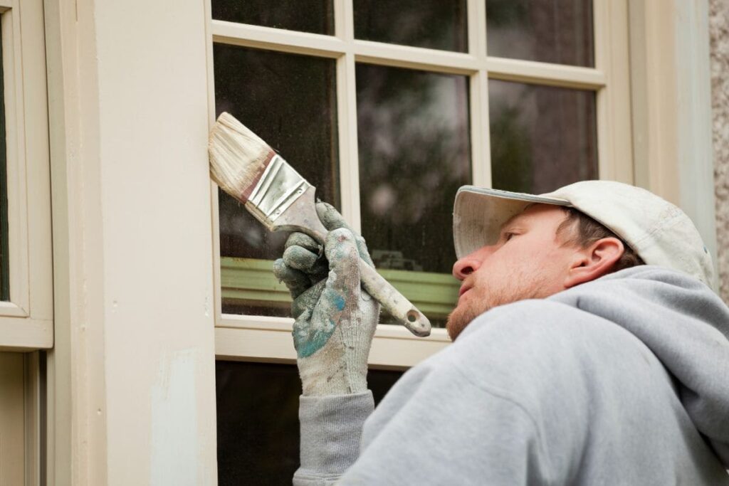 En man målar huset med pensel.